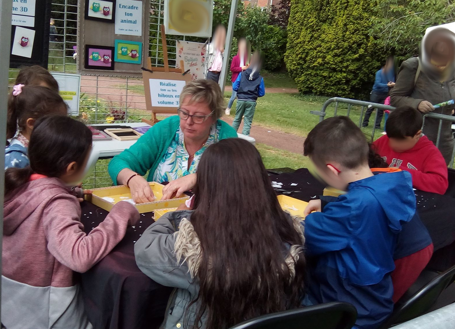 des enfants sont autour de l'animatrice, assis, et creent le sujet choisit par l'organisateur de l'évenement organise dans un jardin botanique.