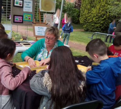 des enfants sont autour de l'animatrice, assis, et creent le sujet choisit par l'organisateur de l'évenement organise dans un jardin botanique.